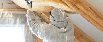 Back view of one foreman in overalls working with rockwool insulation material, fasten warmth layer on ceiling and wall, standing inside new house under construction